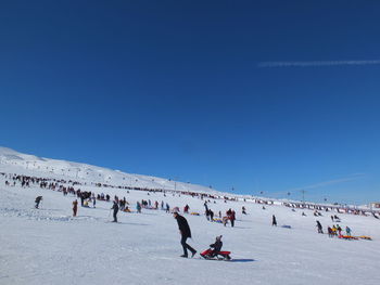 People enjoying in snow against clear blue sky