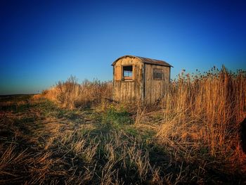 Abandoned house on field against clear blue sky