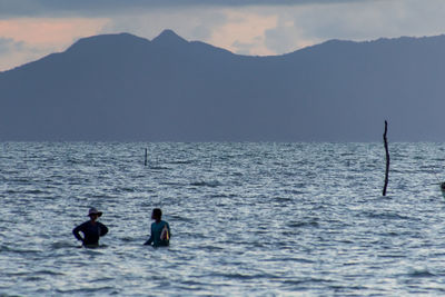 People on sea against mountains