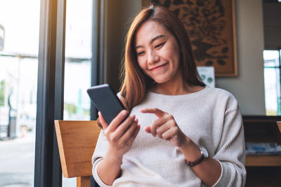 Closeup image of a beautiful young asian woman holding and using smart phone