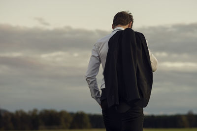 Rear view of man carrying blazer while standing against sky