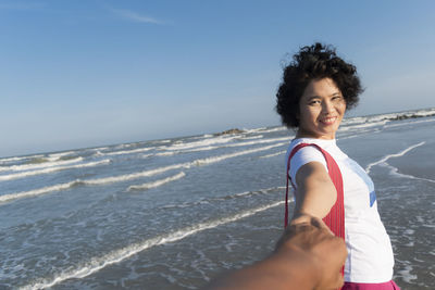 Portrait of smiling young woman on beach against sky