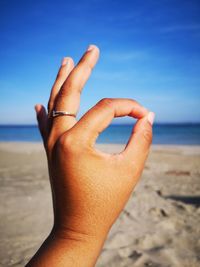 Cropped hand gesturing at beach against clear sky