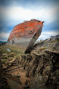 Damaged boat on beach against sky