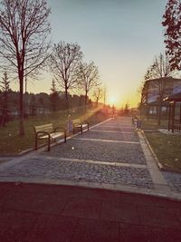 Empty park bench by street against sky during sunset