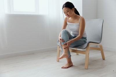 Full length of young woman sitting on chair at home