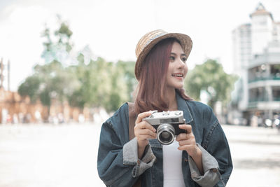 Portrait of young woman photographing against city