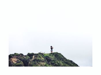 Man standing on cliff by sea against clear sky