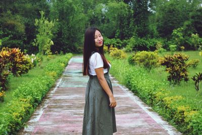 Portrait of young woman standing on footpath at park