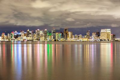 Illuminated buildings by sea against sky