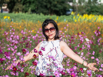 Portrait of smiling woman standing by flowering plants