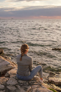 Rear view of woman sitting on rock against sea