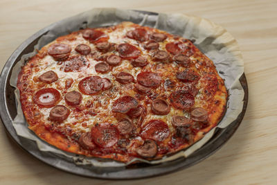 High angle view photography of a homemade pepperoni and sausage pizza on metal tray in wooden table