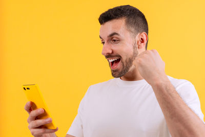 Side view of young man using mobile phone against yellow background