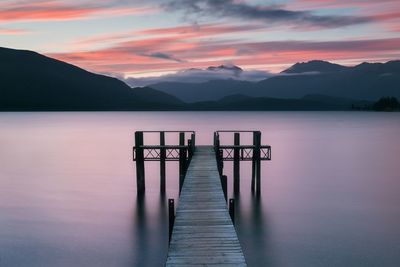 Wooden jetty in lake against sky during sunset