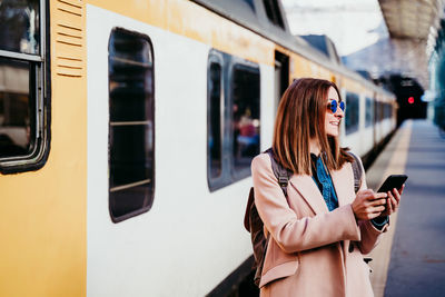 Woman with phone standing by train on railroad station platform