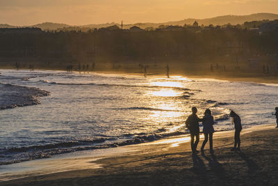 People standing on beach against sky during sunset