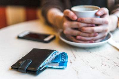 Close-up of hand holding coffee cup on table