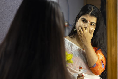 A beautiful indian woman in white saree applying bindi in front of mirror with smiling face