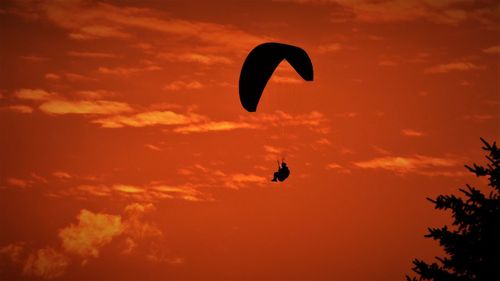 Low angle view of silhouette paragliding against sky during sunset