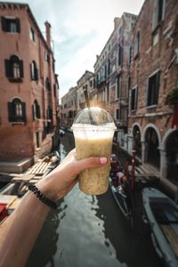 Cropped hand holding disposable cup against canal in city