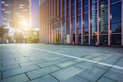 Street by modern buildings against sky during sunset