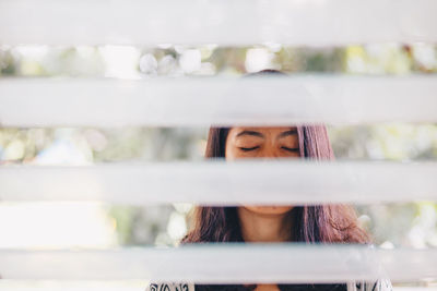 Close-up of woman with eyes closed seen through blinds