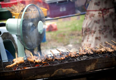 Fried chicken cooks on a grill with a fan behind