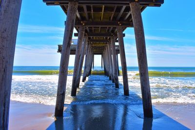 Below view of pier at beach against blue sky during sunny day