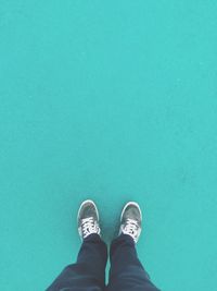 Low section of man standing against turquoise background