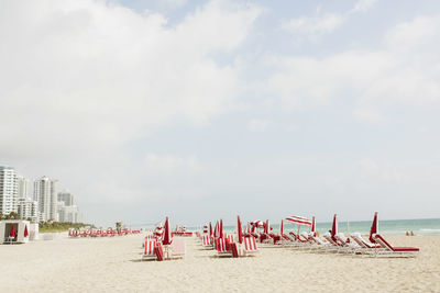 Lounge chairs and parasols at beach against cloudy sky