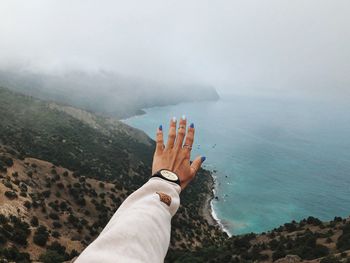 Low section of person hand by sea against sky