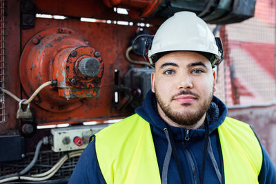 Portrait of confident manual worker standing against machinery in industry