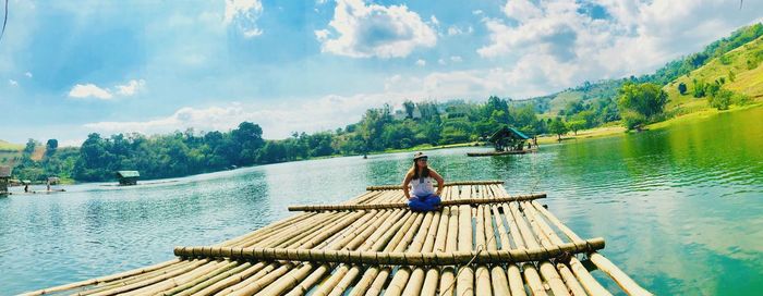 Woman sitting on wood by lake against sky