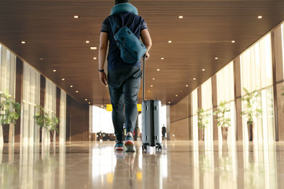 Rear view of man holding suitcase walking in building