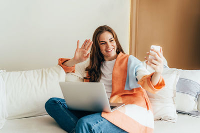 Young attractive redhead woman video chatting on the phone while sitting on the couch at home.