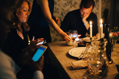 Mature friends using mobile phones while sitting at dining table in dinner party