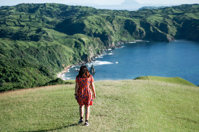 Rear view of woman walking on land against lake amidst mountain