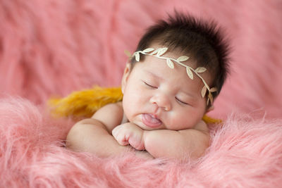 A cute newborn boy wearing a headband and small angle wing sleeping on a pink soft blanket, infant