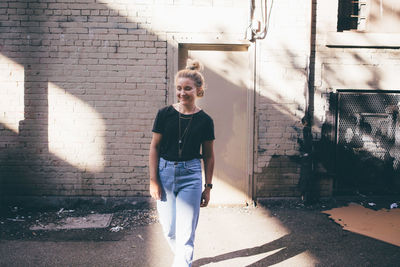 Portrait of smiling young woman standing against brick wall