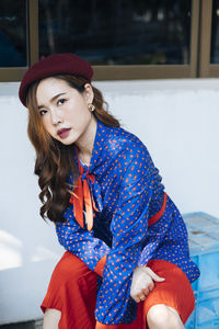 Portrait of young woman sitting against wall outdoors