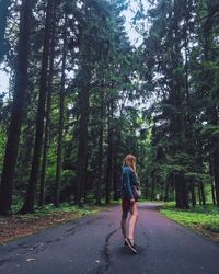 Woman walking on road amidst trees in forest