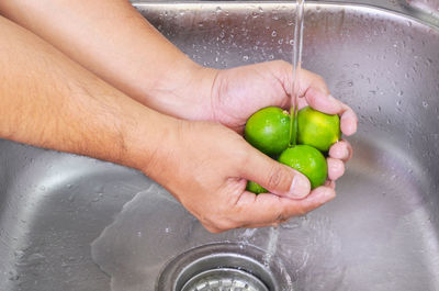 Cropped image of hands cleaning lemons in kitchen sink