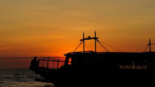 Silhouette boat moored on sea against orange sky