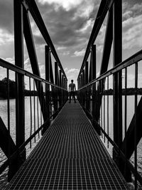 Rear view of man standing on metallic footbridge against sky