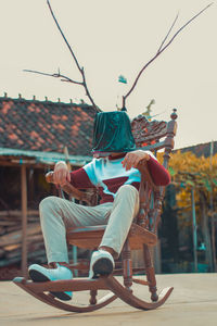 Low angle view of man with pot covered face sitting against sky