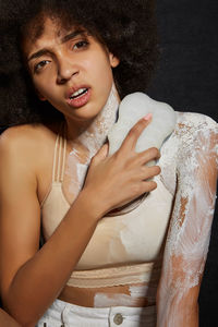 Woman with paint holding sponge while sitting against black background