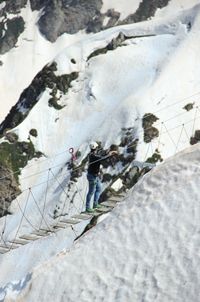 High angle view of man walking on footbridge by snow covered mountains