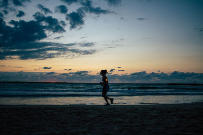 Silhouette man standing on beach against sky during sunset