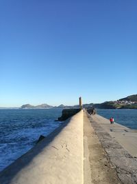 People on pier at sea against clear blue sky